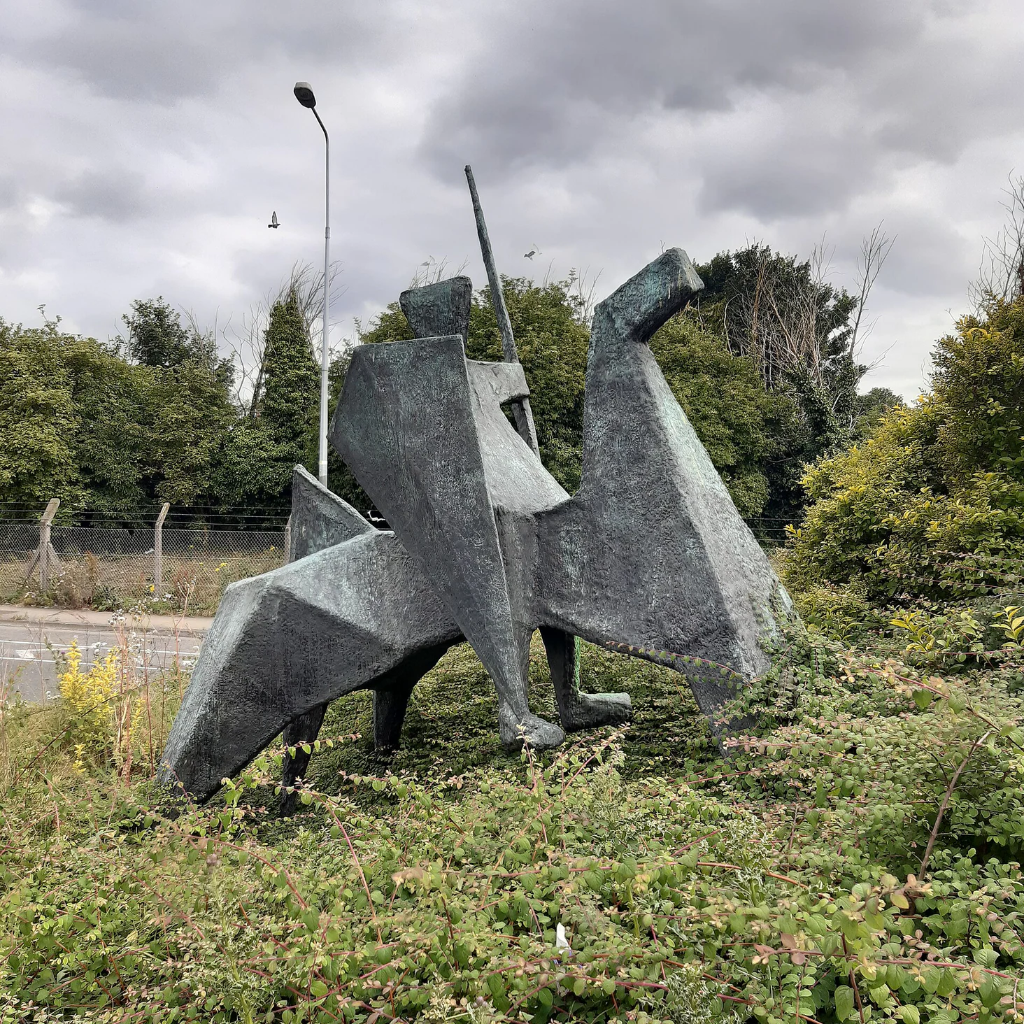 A stone knight sculpture standing on a grass verge beside a Dublin road, with no plaque at its base.