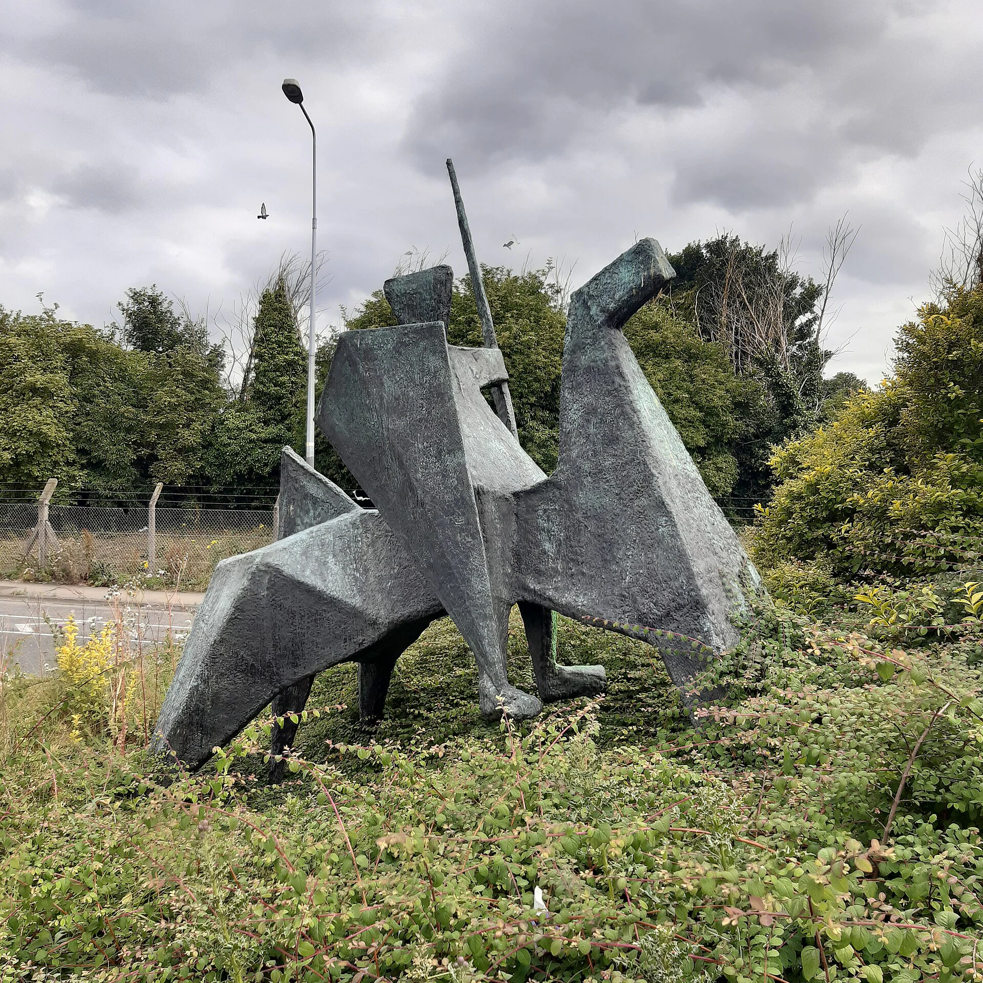A stone knight sculpture standing on a grass verge beside a Dublin road, with no plaque at its base.