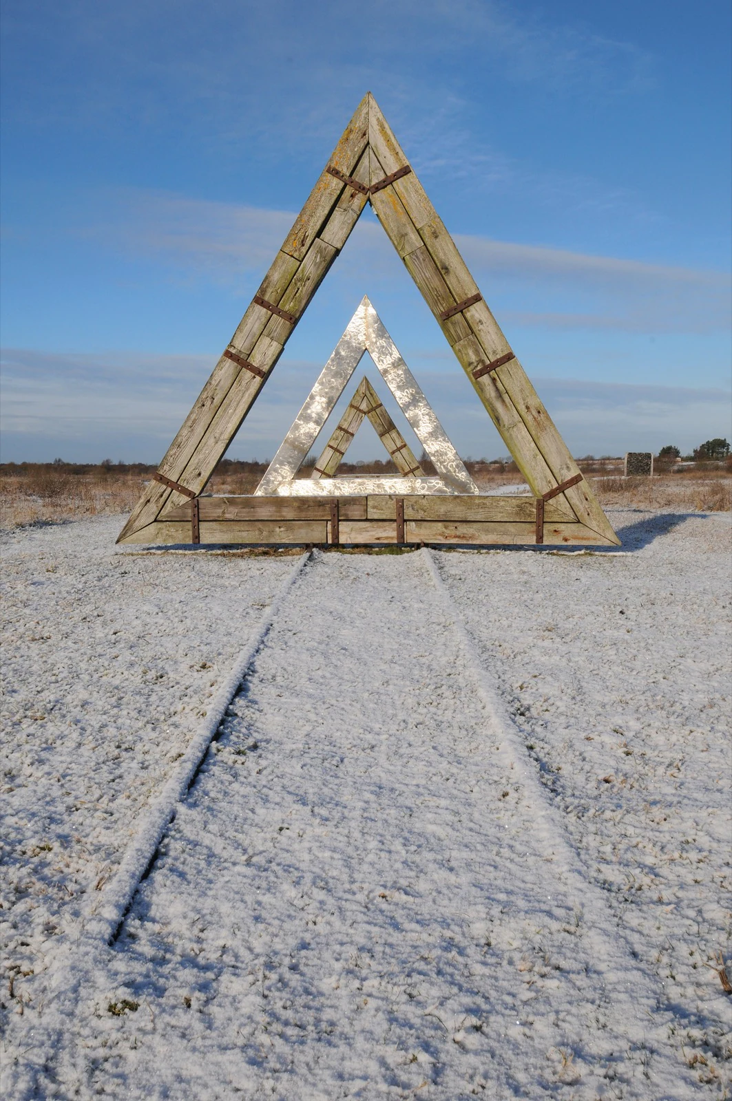 Nested wooden and metal triangles standing in a snowy bog landscape, with a track leading toward them.